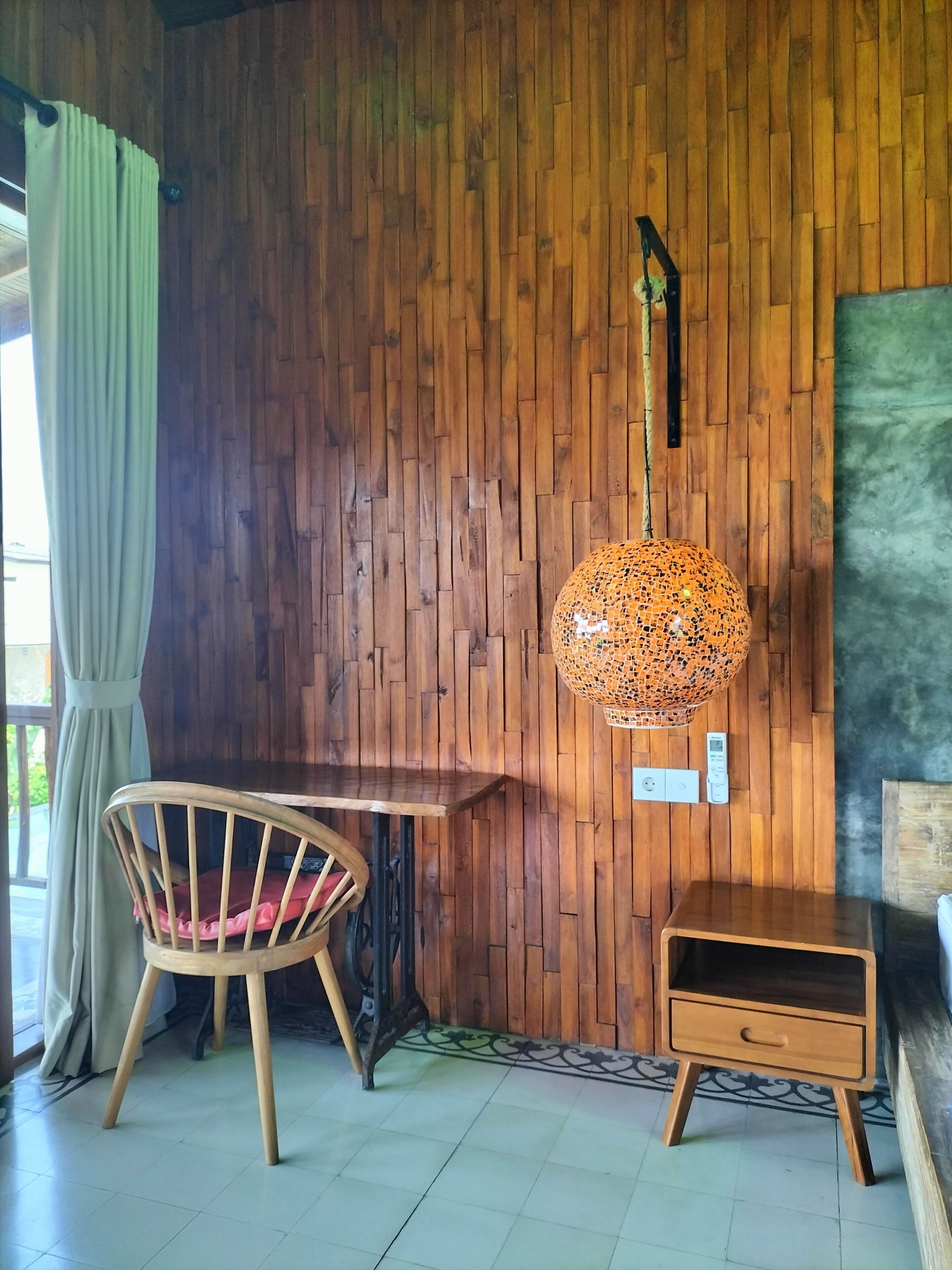 Pared de madera con una lámpara colgante, una silla de madera, una mesita y una mesita de noche.