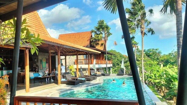 Un espace piscine doté de chaises longues et d’un coin salon abrité, le tout entouré d’une végétation tropicale.