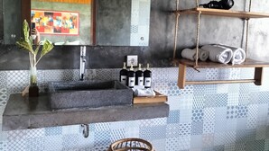 Une salle de bain avec un lavabo en béton, un luminaire suspendu, une étagère en bois avec des serviettes et un panier décoratif.