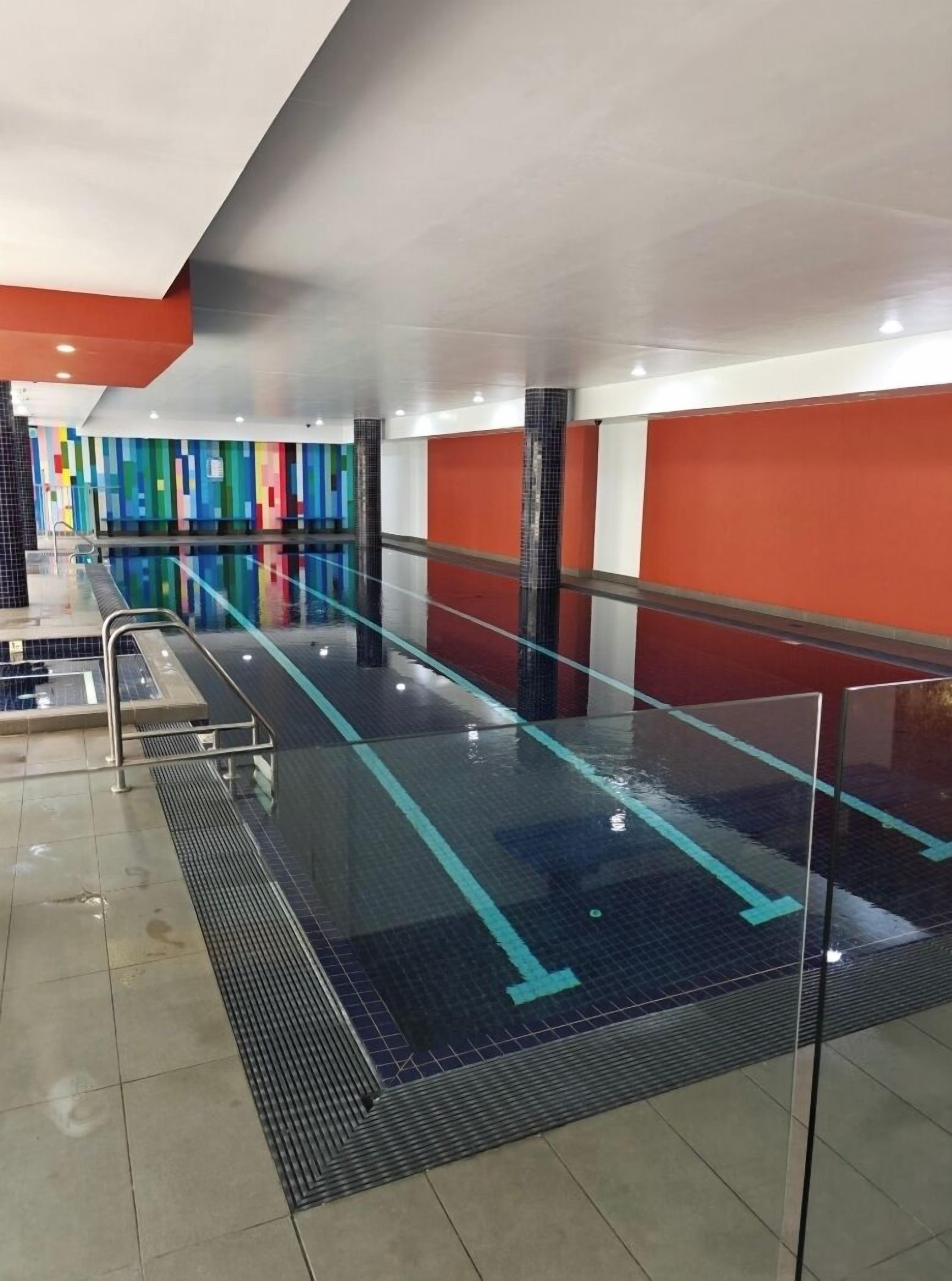 An indoor swimming pool with clear lane markings, a tiled floor, and colorful wall tiles.