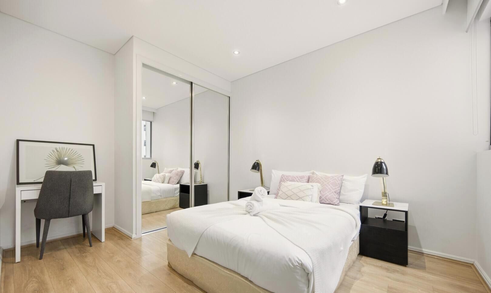 A modern bedroom with a bed, bedside tables, a desk, a chair, and a large mirror.