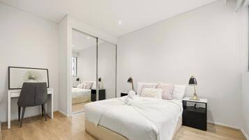 A modern bedroom with a bed, bedside tables, a desk, a chair, and a large mirror.