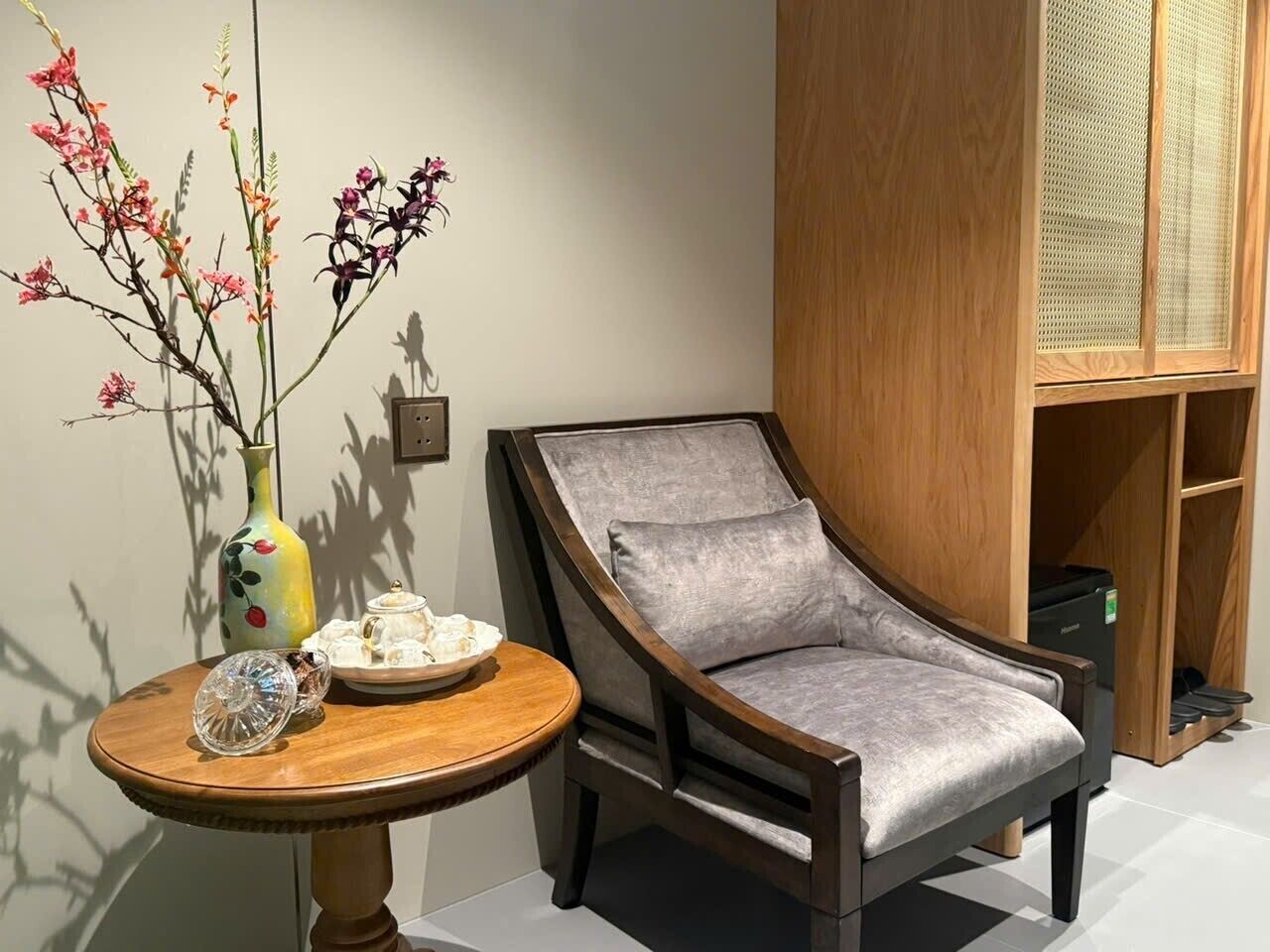 A room with a wooden chair, a round table with a vase of flowers, and a cabinet with a woven basket.