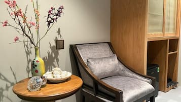 A room with a wooden chair, a round table with a vase of flowers, and a cabinet with a woven basket.