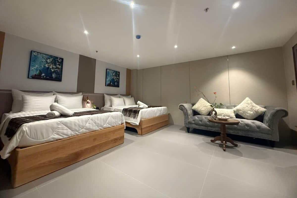 Une chambre moderne avec deux lits en bois, un canapé gris et une petite table ronde.