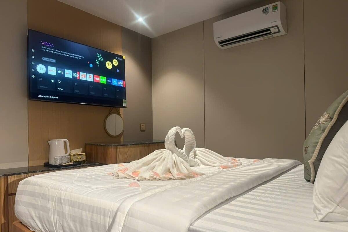 Une chambre d’hôtel dotée d’un téléviseur à écran plat fixé au mur, qui diffuse différents services de streaming. Le lit est recouvert d’une couette blanche et agrémenté d’une composition décorative en forme de cygnes.