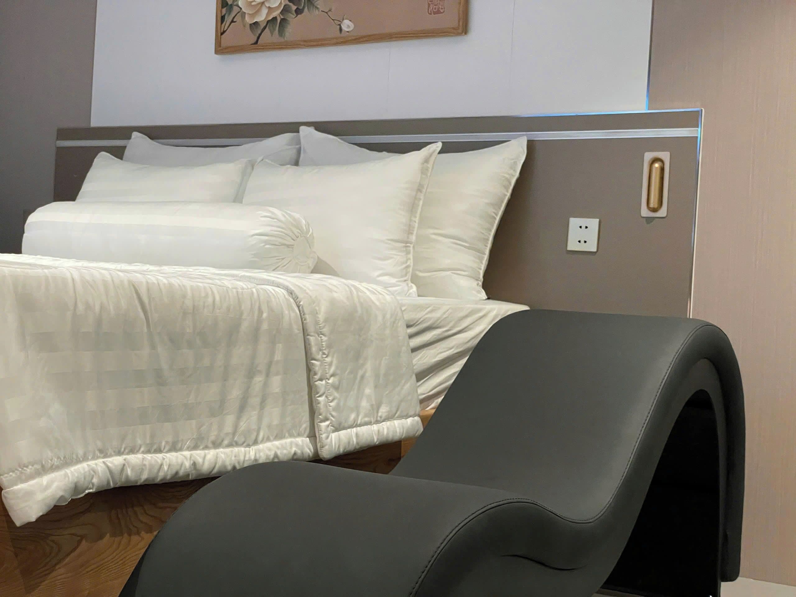 A neatly made bed with white linens and a grey chair in the foreground.