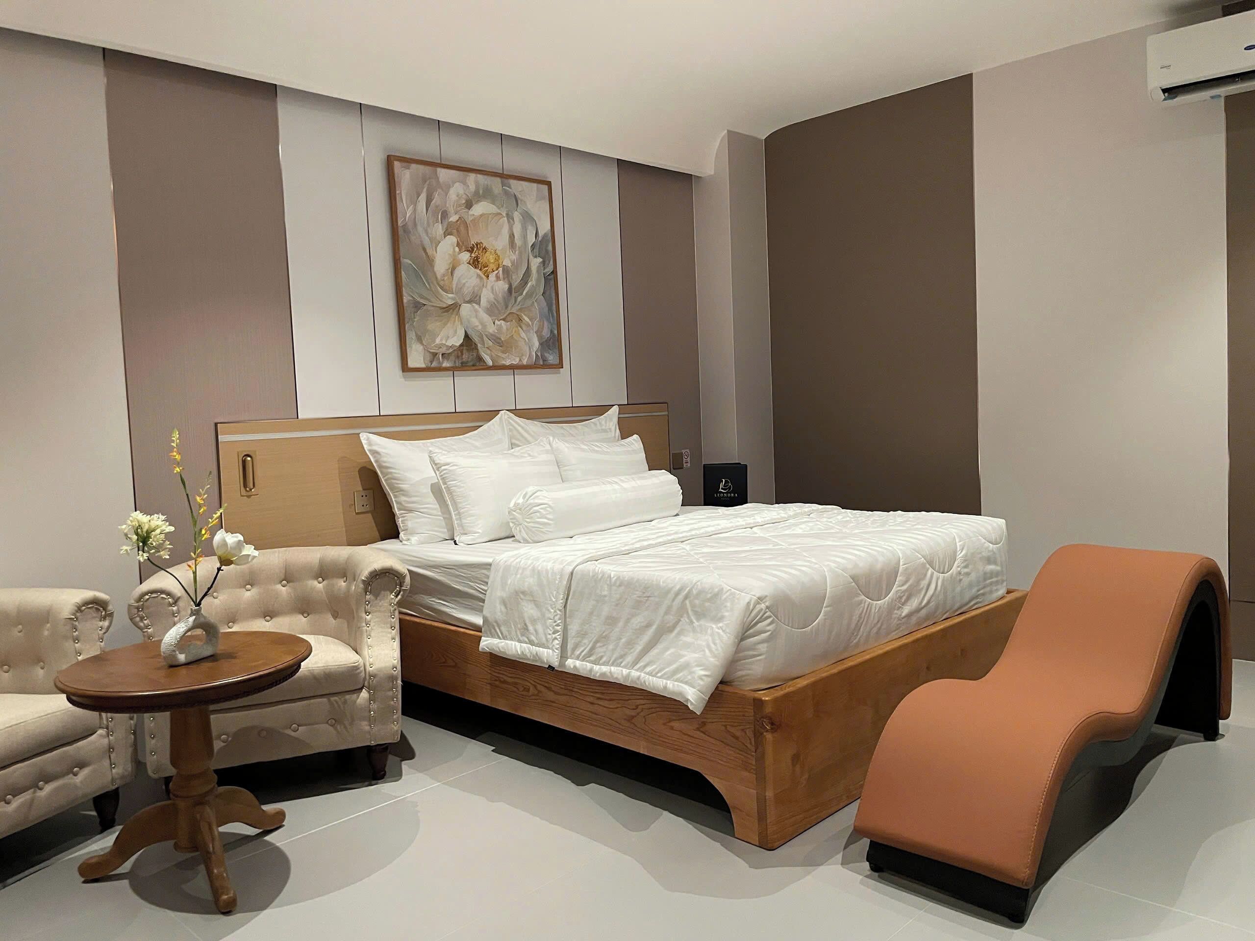 A modern hotel room with a large bed, a sofa, a small table, and a decorative flower arrangement.