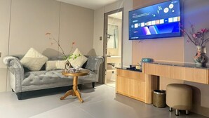 Un salon moderne avec un canapé gris, une table basse ronde en bois et un téléviseur à écran plat fixé au mur.