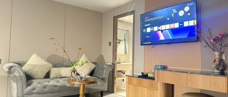 Una sala moderna con un sofá gris, una mesa de centro redonda de madera y un televisor de pantalla plana montado en la pared.