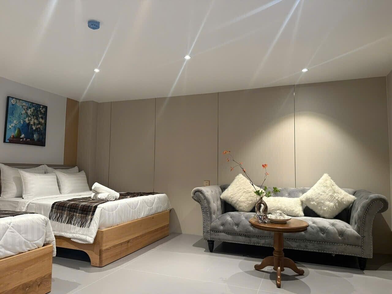 A modern bedroom with a bed, two bedside tables, a grey upholstered sofa, and a small round table with a vase.