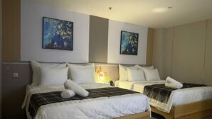 Une chambre d’hôtel avec deux lits, chacun doté de draps blancs et d’une tête de lit en bois. Il y a deux tableaux accrochés aux murs, un petit bureau avec une lampe et une armoire.