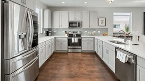 Una cocina moderna con electrodomésticos de acero inoxidable, armarios blancos y suelo de madera.