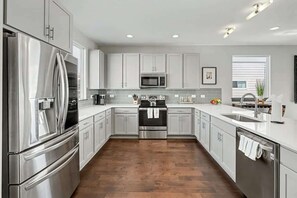 A modern kitchen with stainless steel appliances, white cabinetry, and a wooden floor.