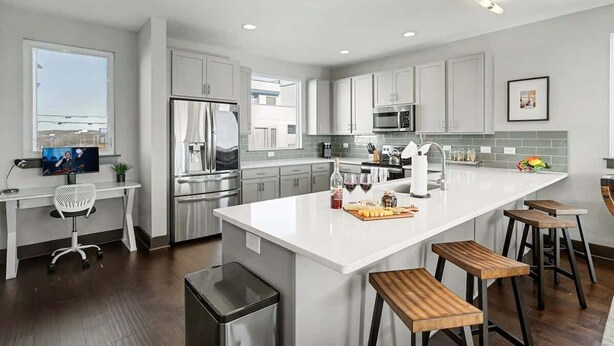Una cocina moderna con armarios blancos, electrodomésticos de acero inoxidable, una isla grande con taburetes y vistas al exterior.