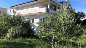 Ein zweigeschossiges Wohngebäude mit flachem Dach, weißen Außenwänden und einem Balkon im oberen Geschoss.