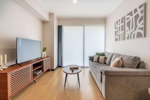 Ein modernes Wohnzimmer mit Flachbildfernseher, einer Holz-Unterhaltungseinrichtung, einem grauen Sofa und einem kleinen runden Couchtisch.