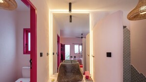 Ein Badezimmer mit einer weißen Toilette, einer rosafarbenen Tür, einem großen Spiegel und einem dekorativen Steinarrangement.