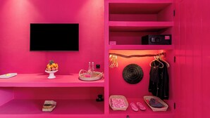 Ein rosafarbenes Zimmer mit einem Flachbildfernseher, einer Obstschale, einem Korb und einem Kleiderhaken.