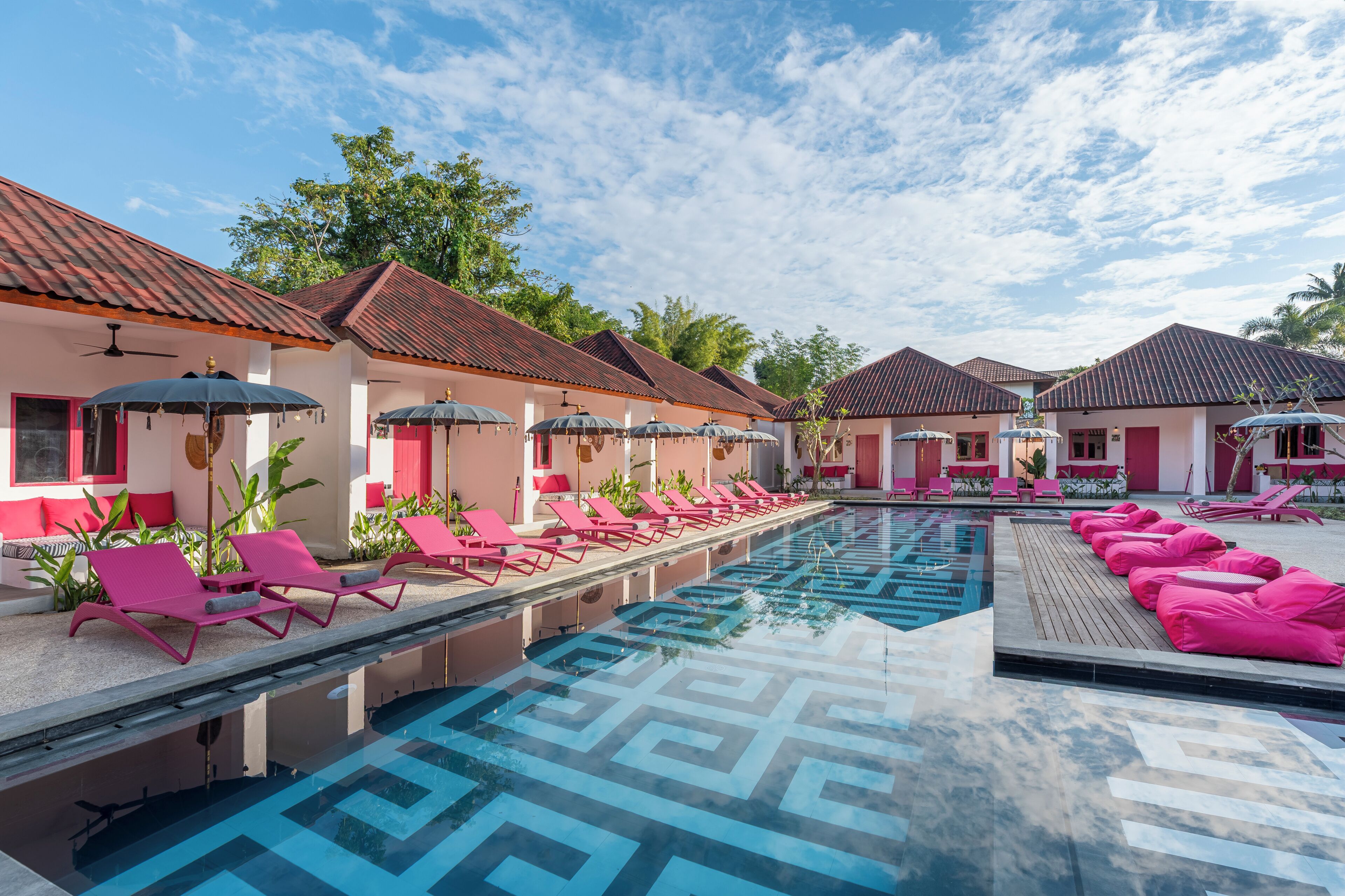 A poolside area with lounge chairs and umbrellas, a clear sky, and buildings with red roofs.