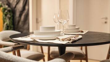 A round dining table with white plates and a wine glass, set with a beige napkin and cutlery.