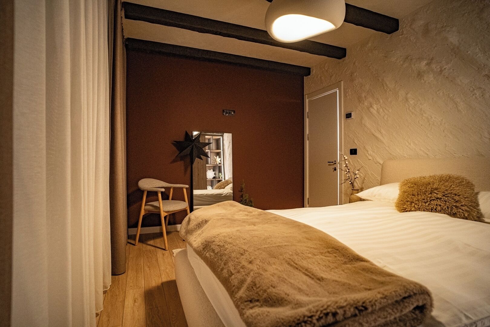 A bedroom with a bed, a chair, a nightstand, a mirror, and a door.