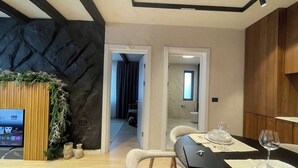 A modern living room with a stone accent wall, a dining area with a black table, and a TV displaying HBO Max. - The Pines Chalet w. free parking (Brașov)