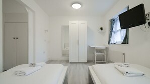 Una habitación de hotel con dos camas, un escritorio, un armario y un televisor montado en la pared.