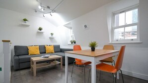 Una sala de estar moderna con un sofá gris, sillones naranjas, una mesa de madera y una ventana con vistas a edificios.