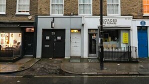 Una hilera de edificios de ladrillo con múltiples ventanas y puertas, incluyendo un escaparate visible con un letrero que dice “GEORGE'S REPAIRS”.