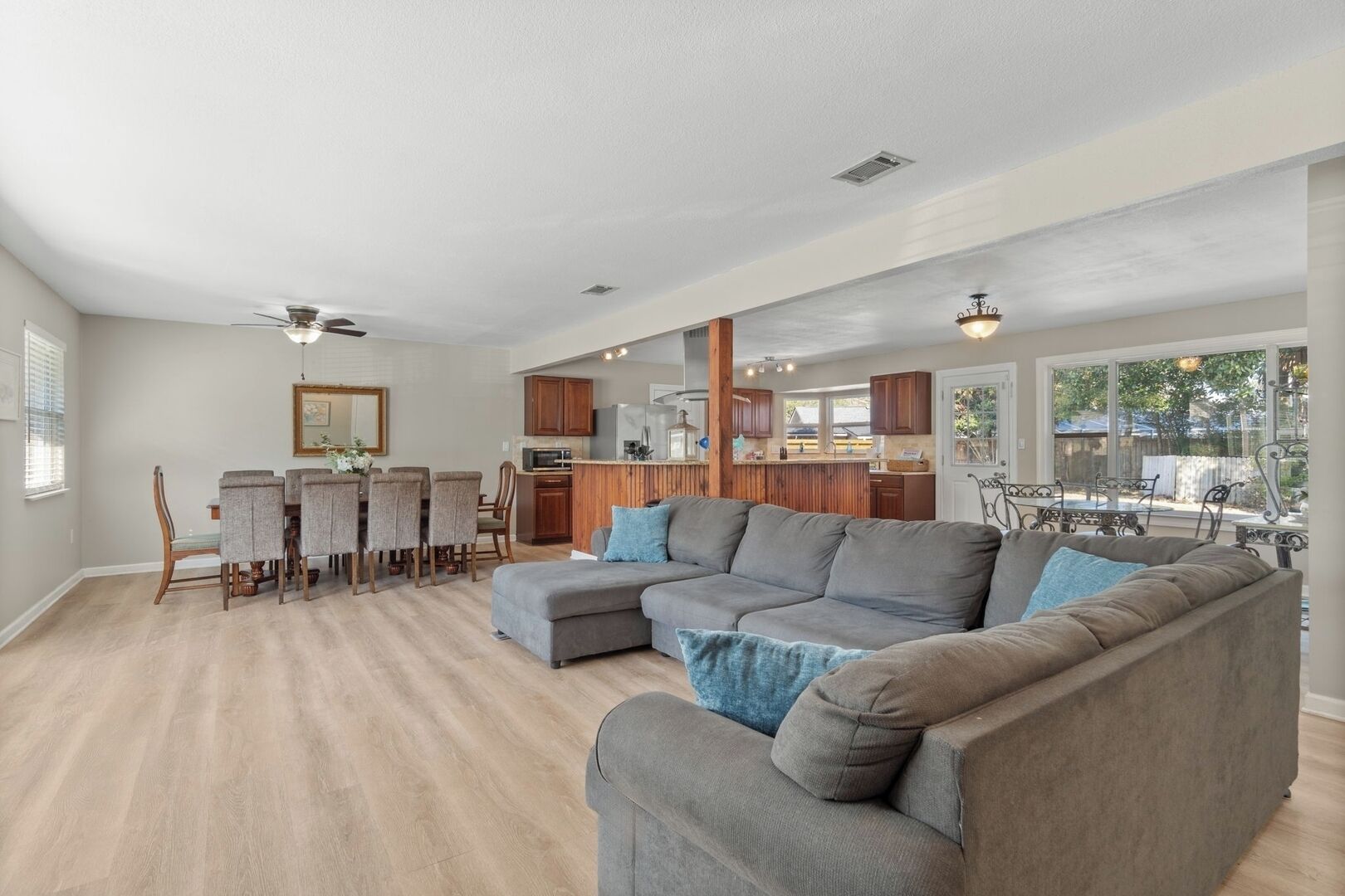 A spacious living room with a large sectional sofa, a dining area with a wooden table and chairs, and a kitchen in the background.