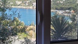 Blick durch ein Fenster auf eine Küstenlandschaft mit Gebäuden, einem Gewässer und einem Bergpanorama.