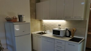 Eine kleine Küche mit weißen Schränken, einer integrierten Mikrowelle, einem Spülbecken und einem Kühlschrank.