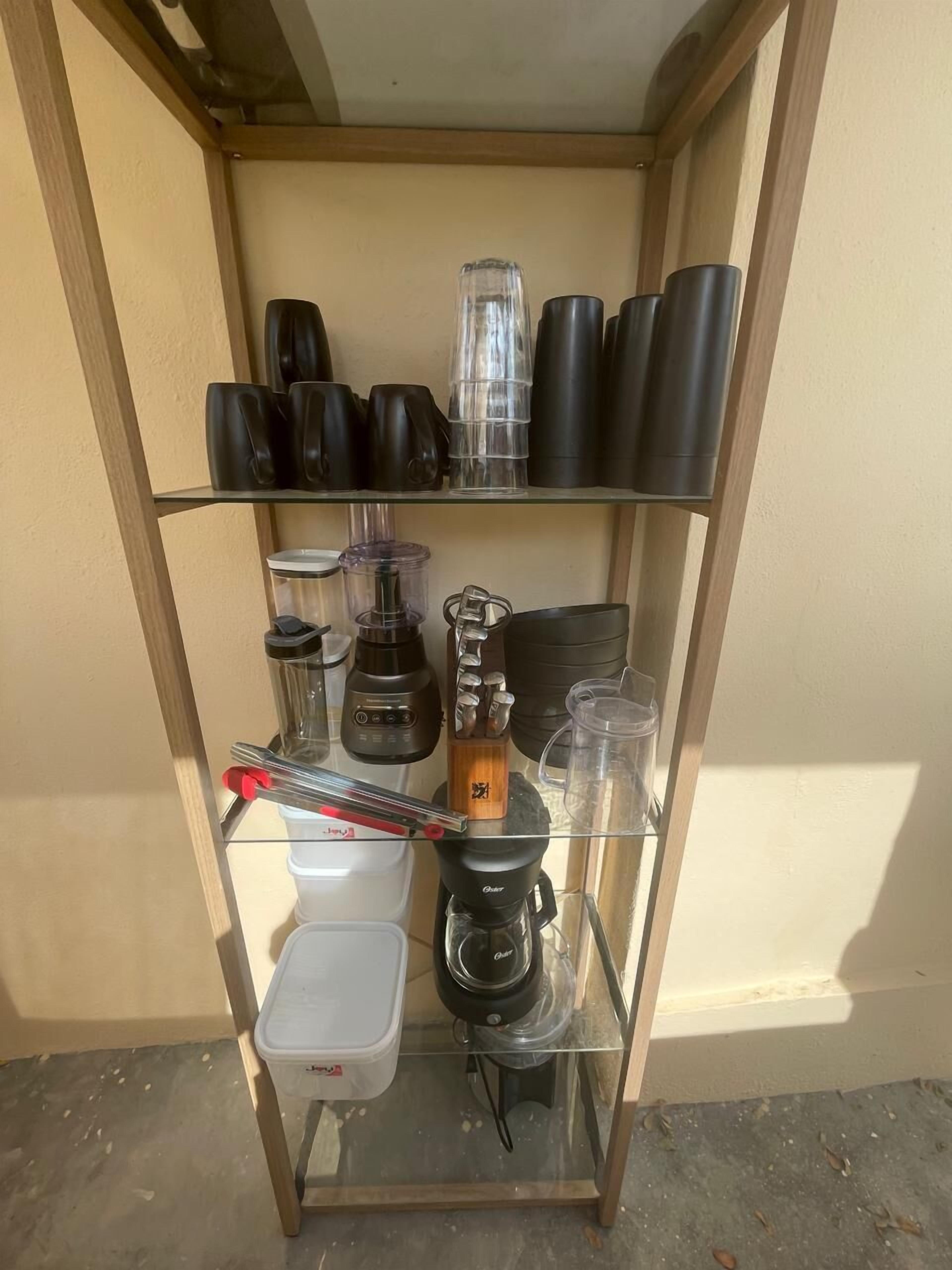 En glashylla med diverse köksartiklar, inklusive en kaffebryggare, en mixer och flera muggar.