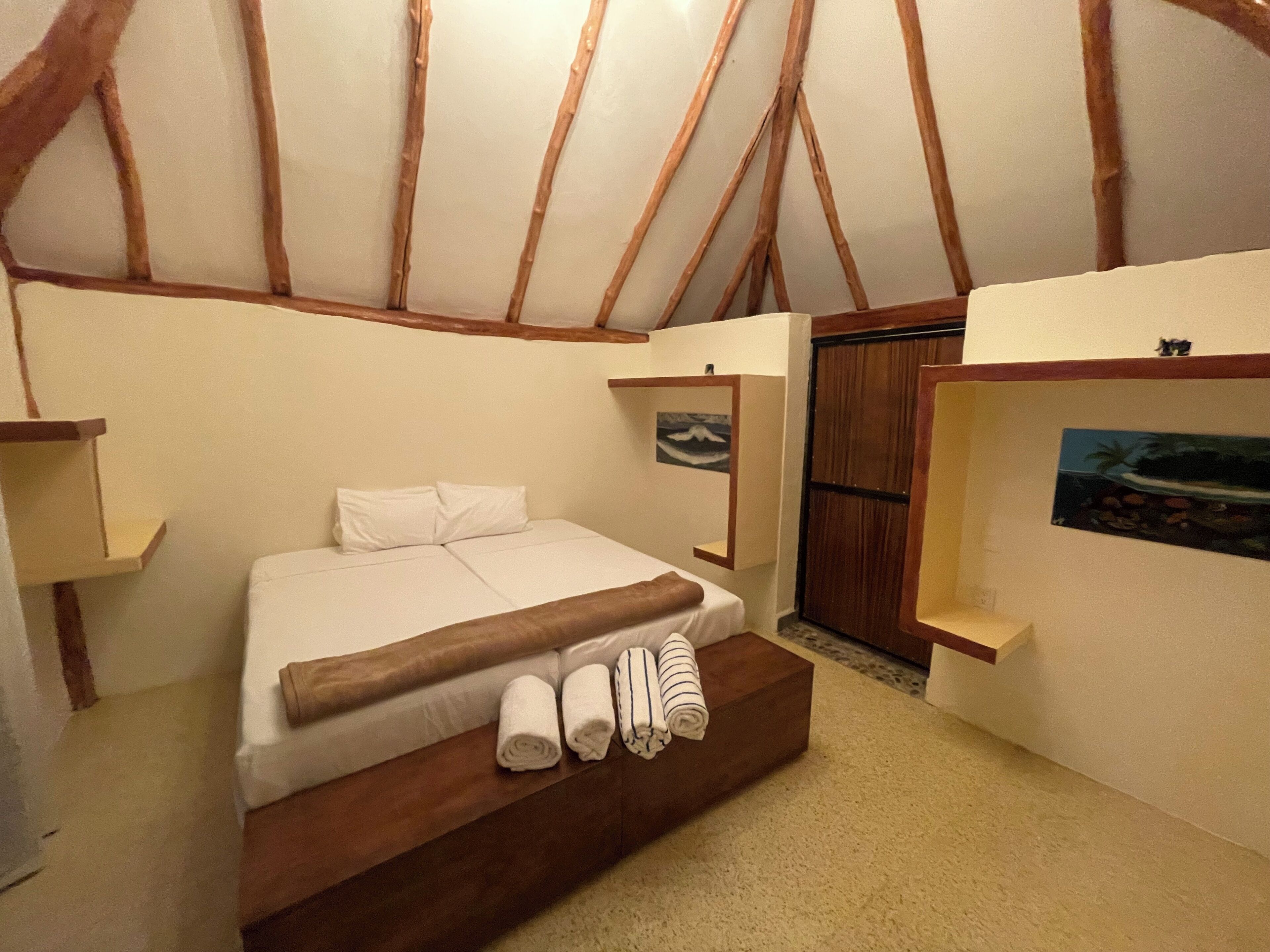 Een slaapkamer met een houten bedframe, een witte matras en twee opgerolde handdoeken.