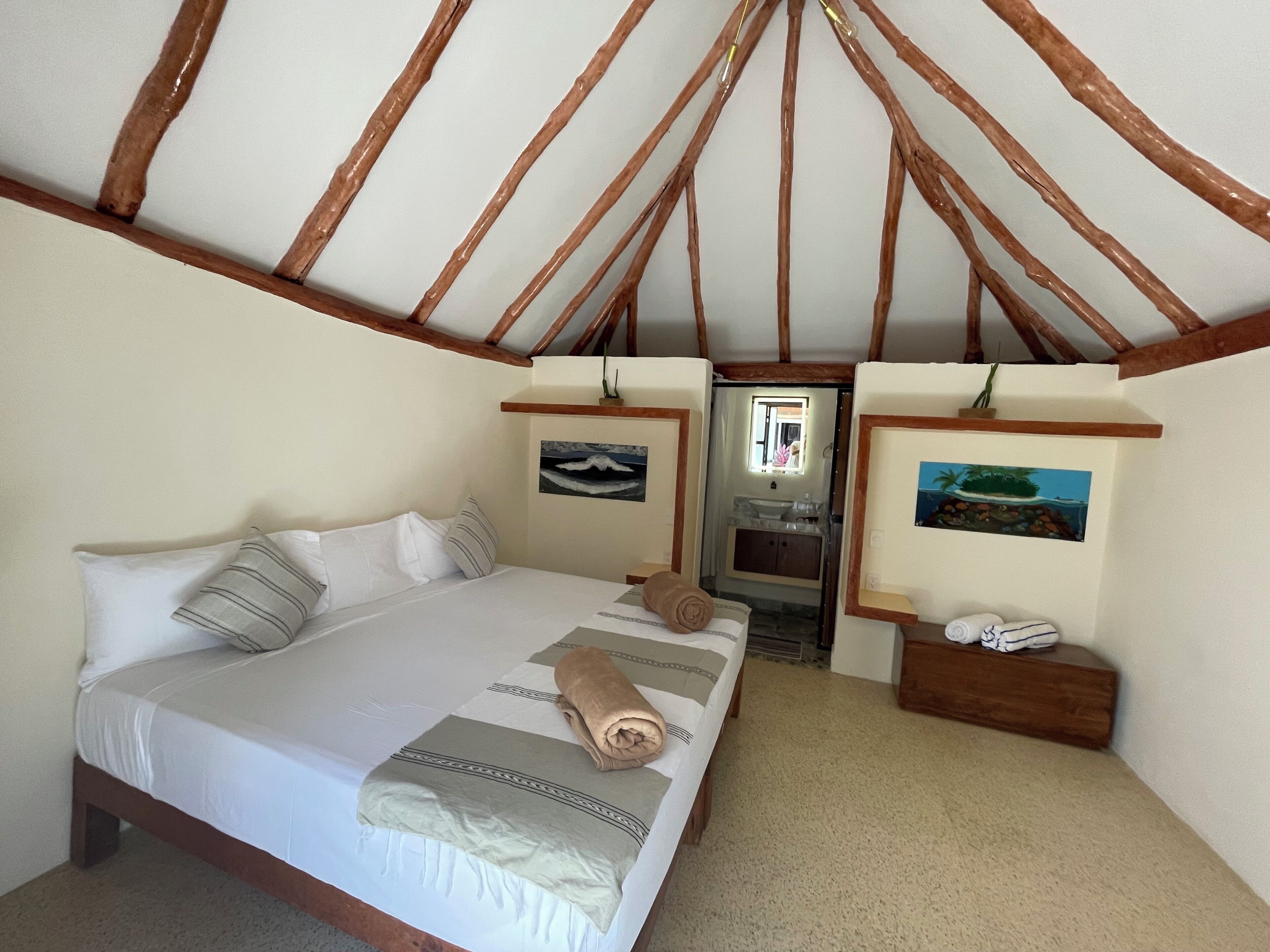 A bedroom with a bed, a nightstand, a mirror, and a painting on the wall.