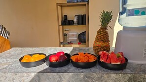 Una encimera de cocina con cuencos de fruta, una piña y un dispensador de agua.