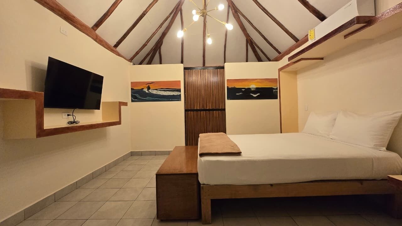 A bedroom with a bed, a TV mounted on the wall, and two paintings on the wall.