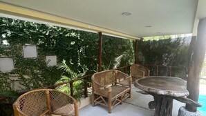 Un patio al aire libre con mobiliario de mimbre, una mesa redonda y una pared decorativa con plantas.