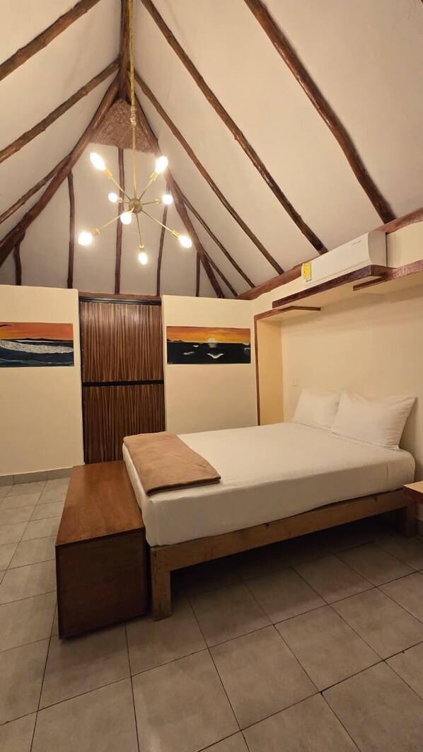 Un dormitorio con una cama de madera, un banco, un ventilador de techo y dos cuadros en las paredes.