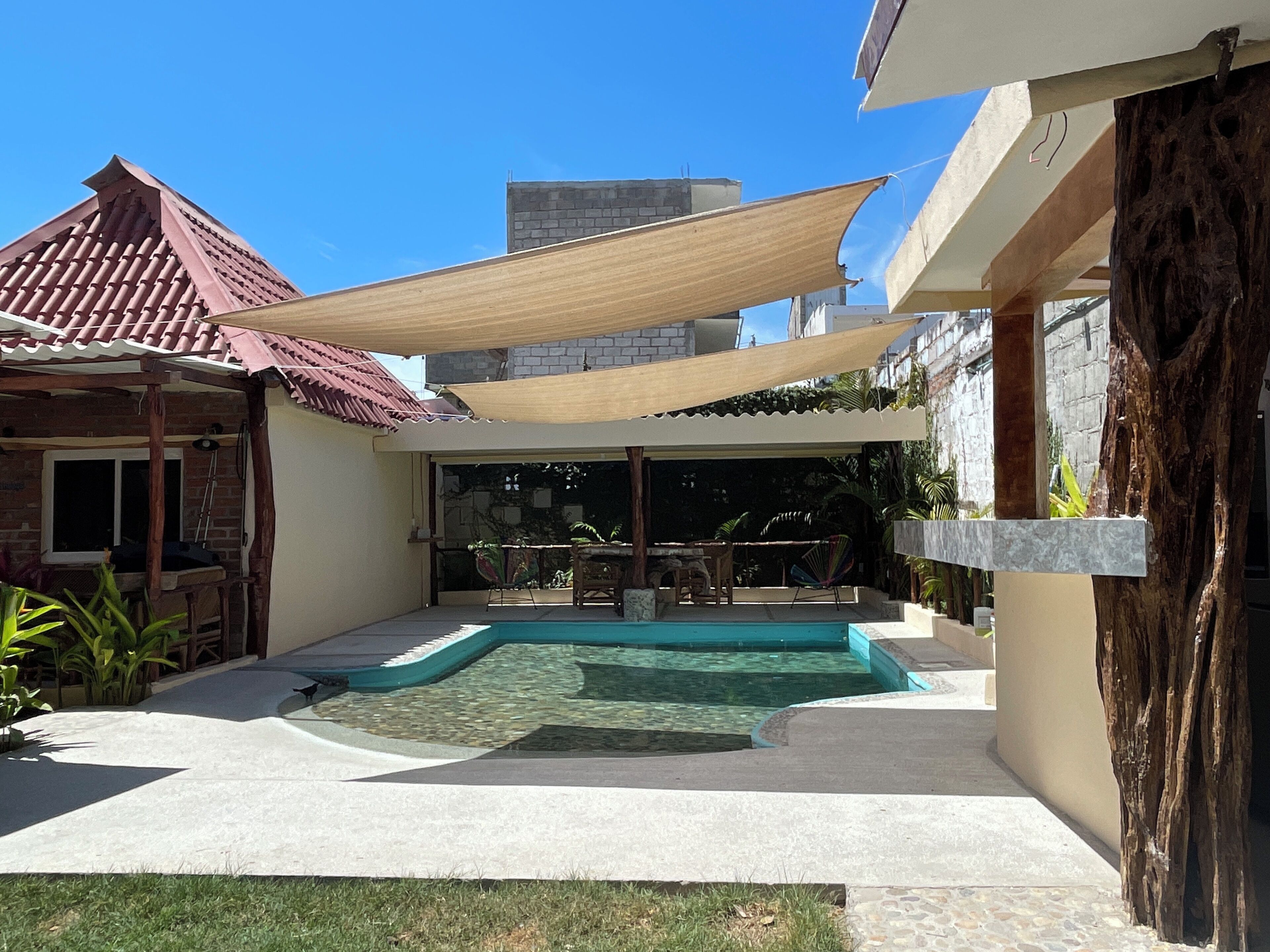 A backyard with a swimming pool, a covered patio, and a stone wall.