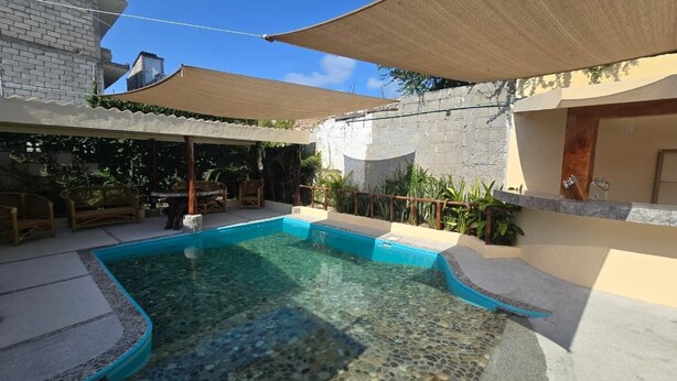 Una piscina con borde de baldosas, rodeada de mobiliario exterior y plantas.