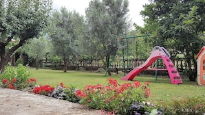 Ein Spielplatz mit einer pinken Rutsche und einer Kletterkonstruktion, umgeben von grünem Gras und blühenden Pflanzen.