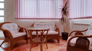 Ein Zimmer mit Korbmöbeln, darunter zwei Stühle und ein kleiner Tisch, sowie eine Topfpflanze.