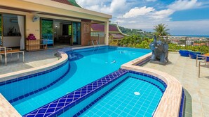 A swimming pool with a curved design, a covered seating area, and a view of a traditional building in the background.