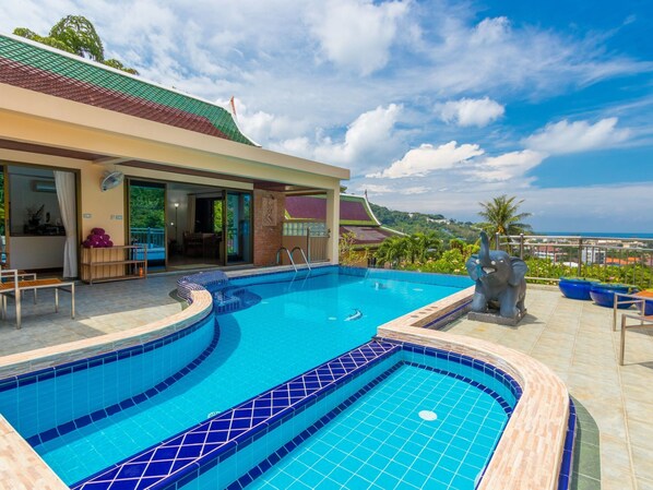 A swimming pool with a curved design, a covered seating area, and a view of a traditional building in the background.