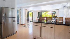 A modern kitchen with a stainless steel refrigerator, wooden cabinets, a glass-top island, and a view of the outdoors.