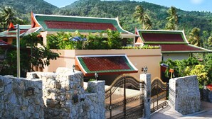 A traditional Thai building with a tiled roof, stone walls, and a gated entrance.