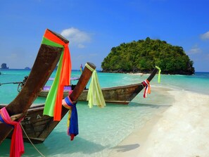 A beach with wooden boats tied to the shore, clear turquoise water, and a small island in the background.