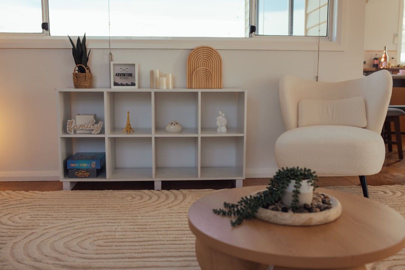 A living room with a white shelving unit, a round coffee table, and a beige armchair.